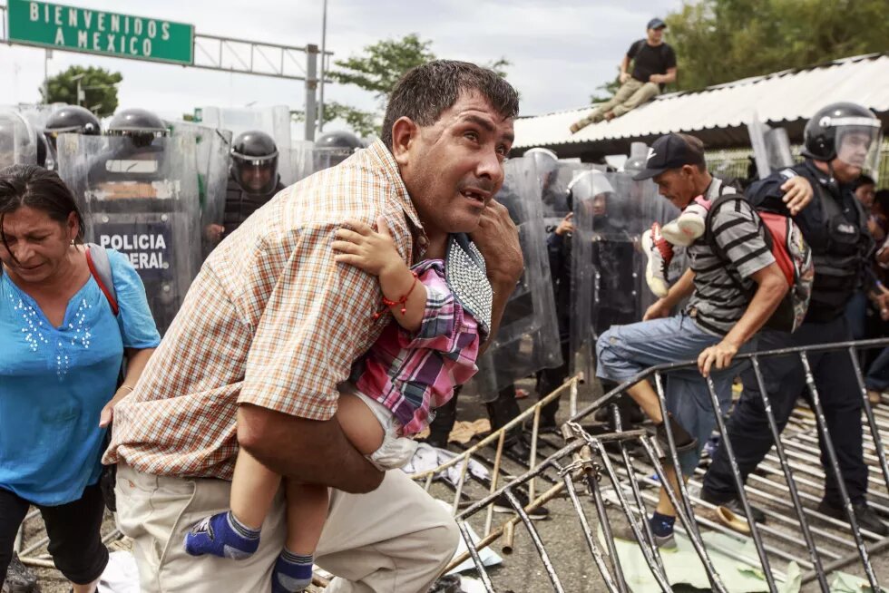 Los éxodos de refugiados en América. Un padre corre despavorido con su hijo en brazos mientras los policías federales disuaden a la multitud de centroamericanos que intentaba ingresar al territorio mexicano tras forzar la apertura del segundo portón.