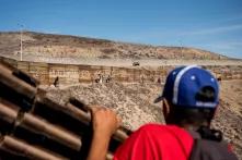 Una columna de migrantes camina al lado del muro, aún del lado meicano. Al fondo, un pick up de la Patrulla Fronteriza estadounidense recorre la frontera.
