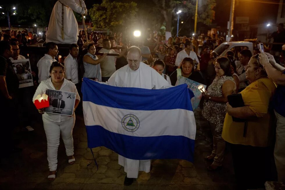 El padre Edwin Román, párroco de la Iglesia San Miguel en Masaya, cargo una bandera de Nicaragua durante la procesión del silencio que se realiza el jueves santo. En la procesión también participaron familiares de los muertos y de los presos políticos. Debido a la labor humanitaria que Román realiza, ha recibido amenazas de muerte, es por eso que desde junio del año pasado posee medidas cautelares por parte de la CIDH. 18 de abril de 2019. Foto: Fred Ramos